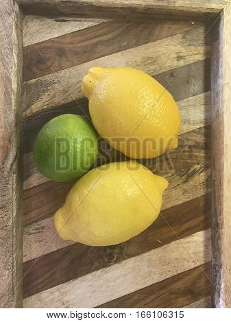 Fresh lemons and a lime on a rustic wood tray in the kitchen.