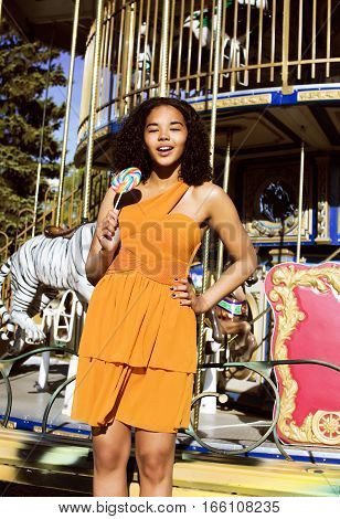 cool real modern teenage girl with candy near carousels at amusement park walking, having fun