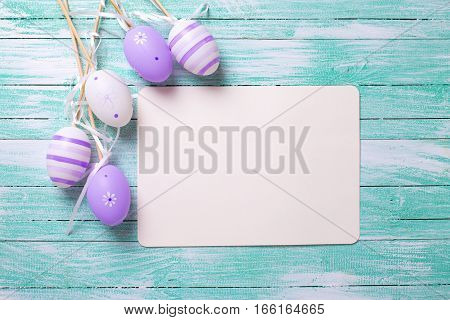 Easter or spring background. Decorative violet eggs and empty tag on turquoise wooden background. Selective focus. Place for text.