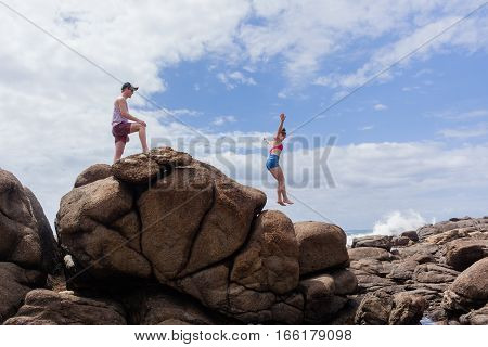 Girl boy mature teenagers exploring jumping beach rocks ocean landscape.