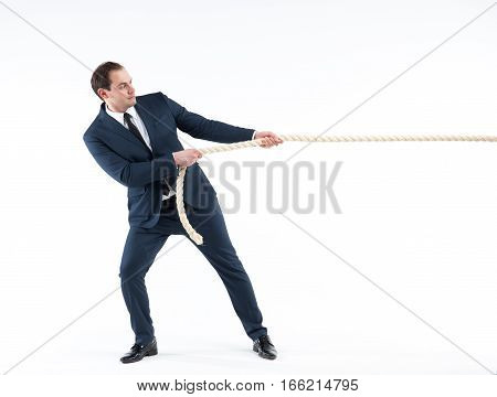 Strong and confident businessman leader. Side view of successful man in suit and tie pulling a rope while standing against white background