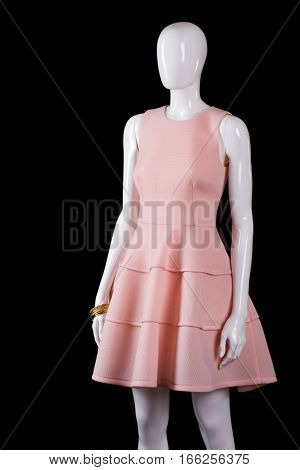 Short evening salmon dress. Light dress on black background. White mannequin wearing stylish dress. Girl's new garment in stock.