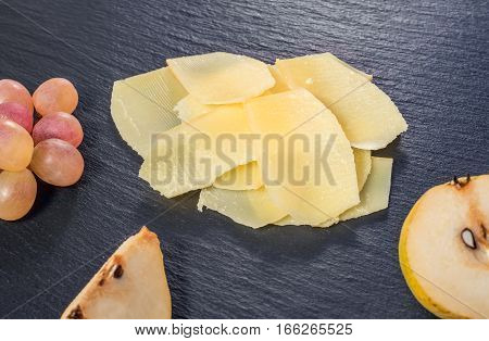 Top View Of Tasty Fresh Yellow Thin Slice Parm Cheese, Cuted Pear And Grapes On Black Stone Slate Ba