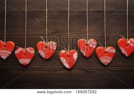 Close up of line of red gingerbreads hearts on ribbon. Festive cookies decorated with sweet sugar mastic for Valentines day. Wooden background.