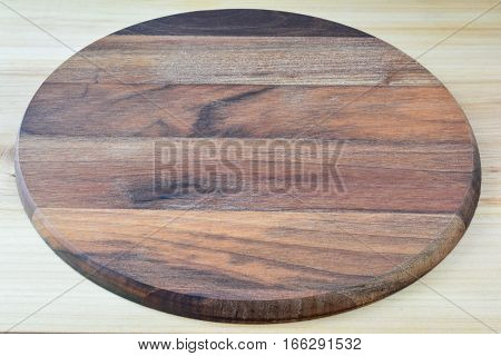 empty round wooden chopping board made from dark nutwood placed on light wooden kitchen table