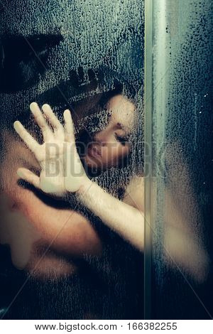 young couple of naked woman and man taking shower with water drops embracing in passion with wet bodies with hand on glass