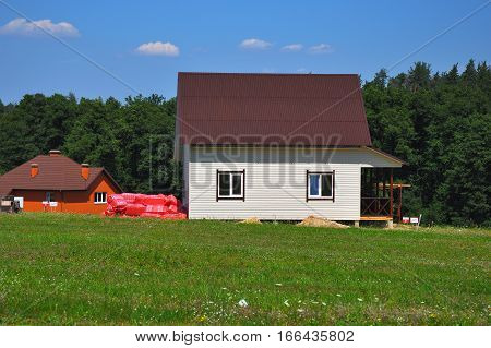 Building beautiful house with siding walls and roofing with asphalt shingles or bitumen tiles near forest in cozy cottage town