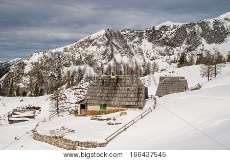 Scenic wooden herdsmen cottages on snowy alpine meadow