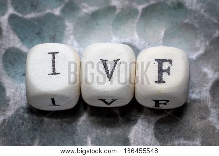 the word ivf (in vitro fertization) lined with wooden blocks on a metal forged textural background.
