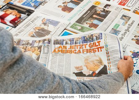 PARIS FRANCE - JAN 21 2017: Man readingmajor international newspaper journalism featuring news Donald Trump America First inauguration as the 45th President of the United States in Washington D.C and relatiosn with Vladimir Putin