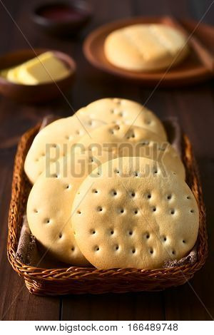 Traditional Chilean Hallulla bread rolls in basket butter and jam in the back photographed on dark wood with natural light (Selective Focus Focus on the first roll)
