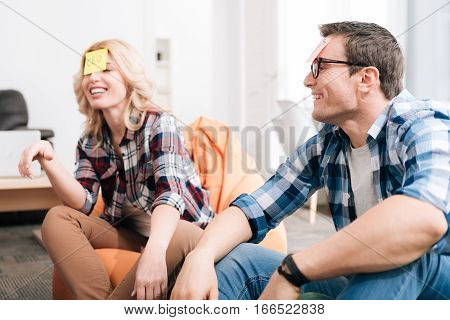 Guess my job. Delighted good looking nice man and woman wearing sticky notes on their foreheads and playing a name game while resting with their colleagues