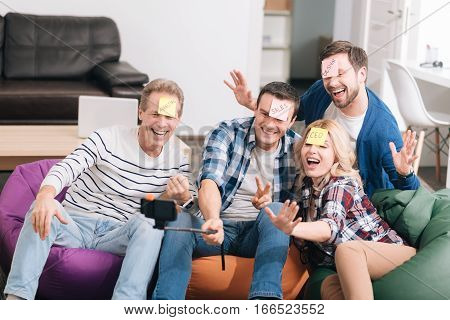 Moment to remember. Cheerful happy positive colleagues having sticky notes on their foreheads and posing for a photo while taking a selfie