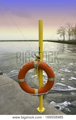 Emergency life preserver hanging on a yellow pole by an icy winter lake at sunset
