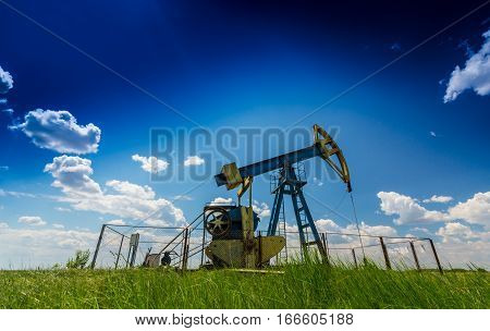 Oil field with pump jack, profiled on blue sky with white clouds, on a sunny day