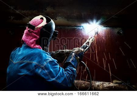 Steel welder with protective mask welding metal and sparks.