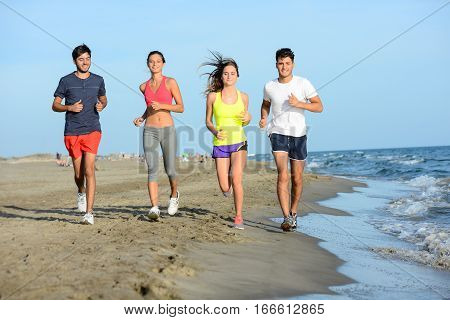 group of young people running in the sand on the shore of a beach by the sea at sunset during a sunny summer holiday vacation