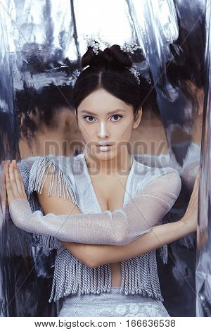 Portrait of futuristic young woman. Reflection of our mind and soul concept. Beautiful young multi-racial asian caucasian model cyber girl in silver urban clothes with conceptual hairstyle and make-up in metallik silver capsule.