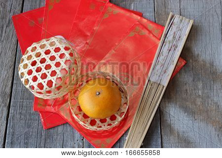 Top view of orange in a basket on old wooden board with Chinese red envelope packet or ang pao and hand blow background. Happy Chinese new year concept.