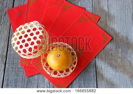 Top view of orange in a basket on old wooden board with Chinese red envelope packet or ang pao background. Happy Chinese new year concept.