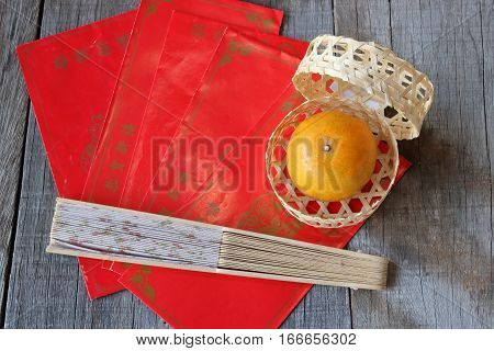 Top view of orange in a basket on old wooden board with Chinese red envelope packet or ang pao and hand blow background. Happy Chinese new year concept.