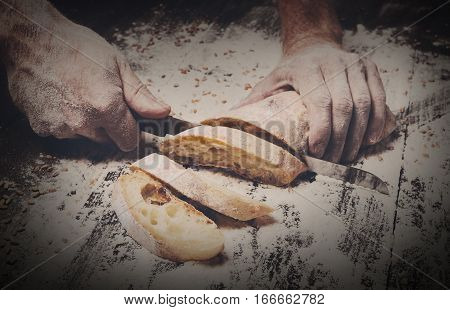 Baking and cooking concept background. Hands cutting bread loaf with knife on rustic wooden table sprinkled with flour. Stained dirty hands of baker.
