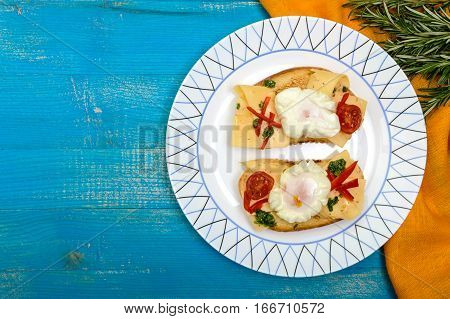 Crispy toast with poached egg cheese peppers tomatoes souse on a plate on a blue background. The top view.