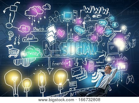 Young businessman sitting on chair with hands on head and socia communication concept on wall