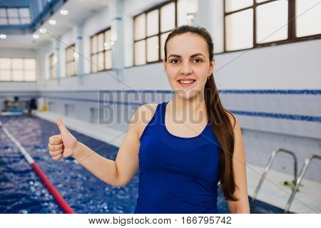 Portrait woman swimming coach in a sportswear showing thumbs up, which is in the workplace, swimming pool