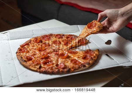 Pizza with salami and cheese. In the hand a slice of pizza
