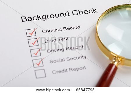 High Angle View Of Magnifying Glass Over Background Check Form