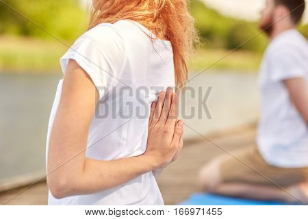 fitness, sport, yoga and healthy lifestyle concept - group of people exercising in reverse prayer pose on river or lake berth