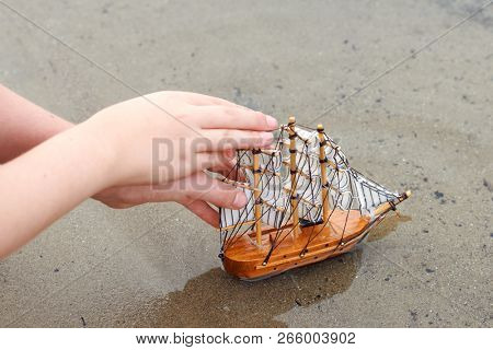 girl playing with a toy sailing ship by the river, hand closeup
