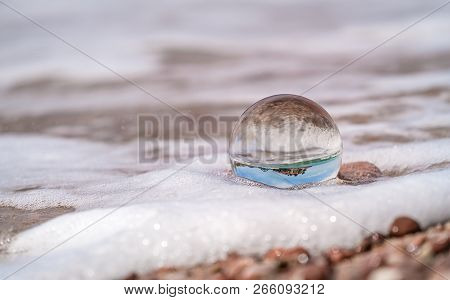Large Transparent Glass Ball Half Submerged By The Incoming Waves On The Beach, Coast Of Montenegro