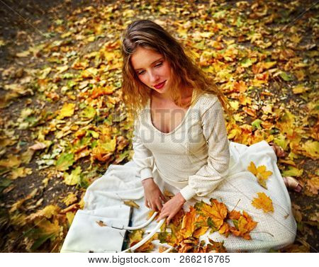Autumn fashion feminity lace dress with long sleeve in princess style. Top view of girl model trew foliage bouquet sitting gracefully and flirt see on fall leaves in city park outdoor.