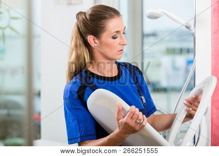 Female maintenance worker checking the quality of a white toilet seat in the showroom of a sanitary ware shop with modern fixtures and accessories 