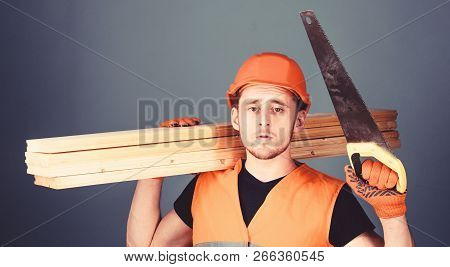 Man, Handyman In Helmet, Hard Hat Holds Handsaw And Wooden Beams, Grey Background. Carpenter, Woodwo