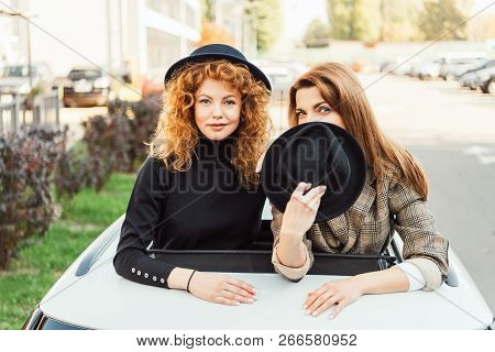 Attractive Fashionable Women Posing And Leaning Out From Car Hatchway At Urban Street