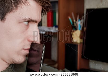 Thoughtful Guy With A Smartphone At His Mouth, Sits At His Desk, On A Black Monitor Background