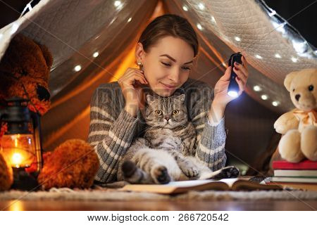 Beautiful Girl In A Dark Room With A Cat In A Tent Reading A Book With A Lantern