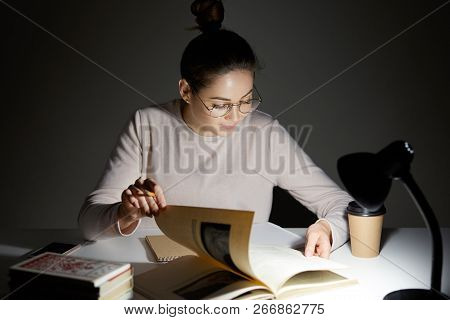Photo Of Serious Female Sudent Turns Over Pages In Book, Searches Necessary Information For Writing 