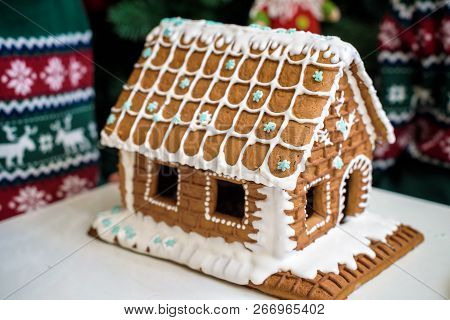 Homemade Christmas Gingerbread House In The Snow. Decorated Christmas Tree In The Background.