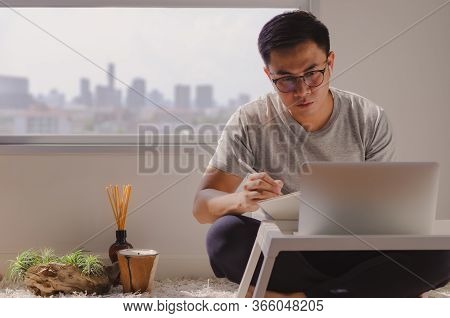 Asian Man In Casual Wear Sitting And Working On Laptop In Room That Have Candle, Aroma Diffuser And 