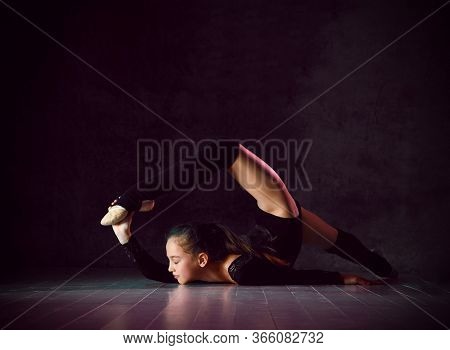 Young Girl Gymnast In Black Sport Body And Uppers Lying On Floor On Neck With Streched Back And Body