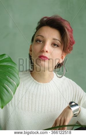 Beautiful Lady In White Sweater, Silver Earrings, And Braclet Sitting Near Green Palm Tree And Looki