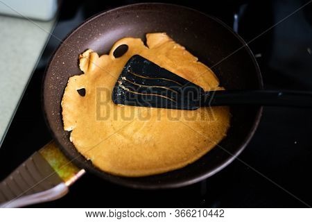 Pancake On A Frying Pan. There Is A Black Spatula On The Pancake