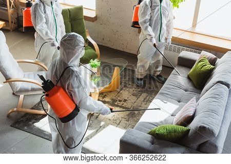 Coronavirus Pandemic. A Disinfectors In A Protective Suit And Mask Sprays Disinfectants In House Or 