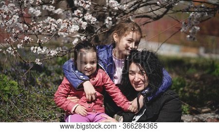 Mom With Two Cute Daughters In A Park Near A Flowering Tree In Spring. Concept Of Happy Family And S