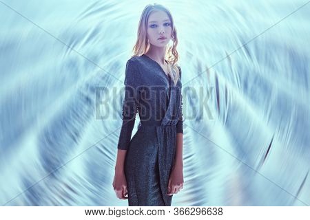 Beautiful blonde model girl in a dark sparkling dress with lurex posing in the light of softbox. Beauty, fashion.