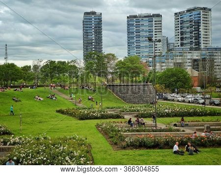 Tade In A Crowded Green Square With Buildings In The Background